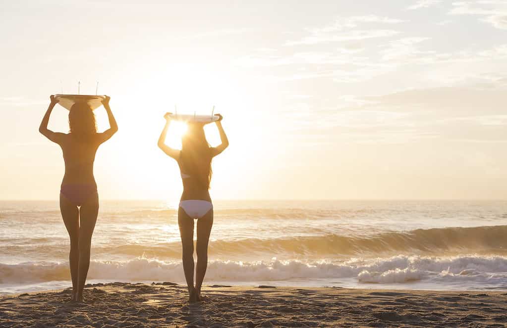 A girl with a surfboard ontop of her head walking to the beach