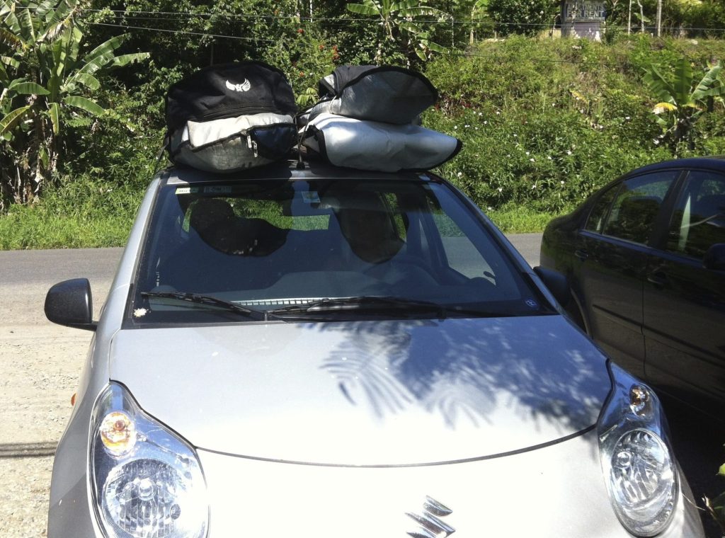A small car in Costa Rica with a lot of surf boards on the top of it.